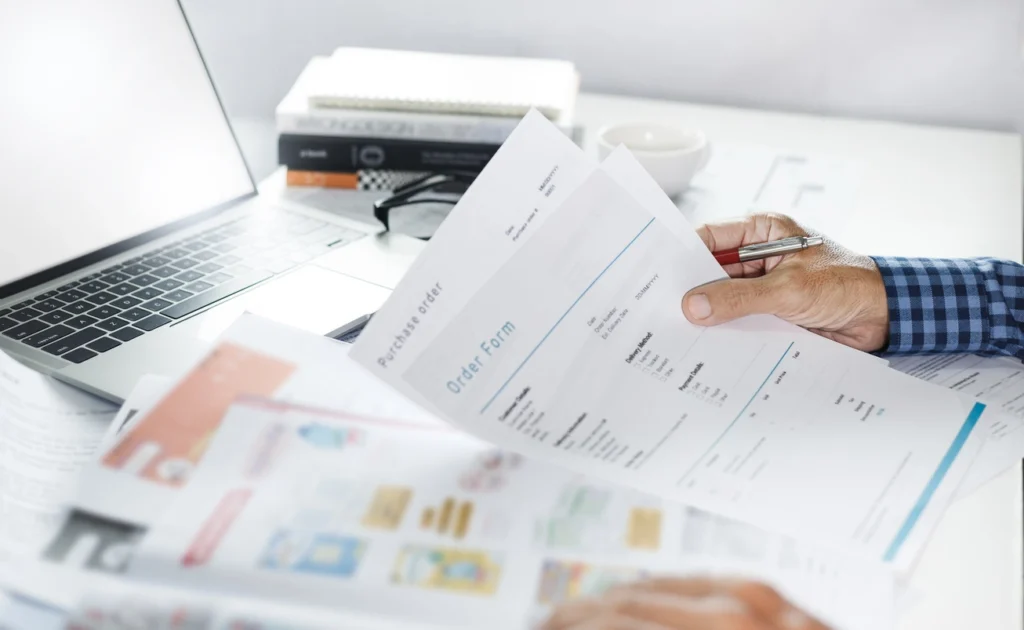 a man holding an order form and laptop and books in the table